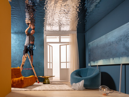 Ein Mann steht auf einer Leiter und bringt eine blaue Leuchte an die Decke an.