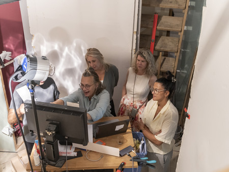 Es sind fünf Personen zu sehen, die um einen Computerbildschirm versammelt sind. Eine Person sitzt am Tisch und schaut auf den Bildschirm, während die anderen Zuschauer hinter ihr stehen. 