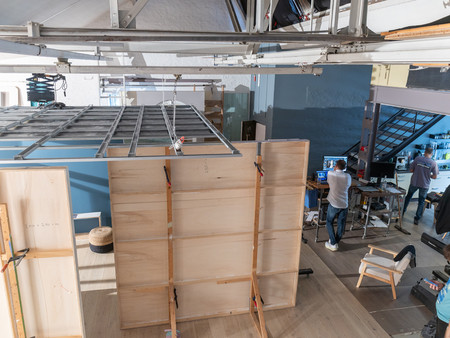 Ein Blick auf einen offenen Raum mit flexibler Struktur. Im Vordergrund sind große, mobile Holzwände aufgebaut,  die Teil eines Setups für eine Fotoproduktion sind. 