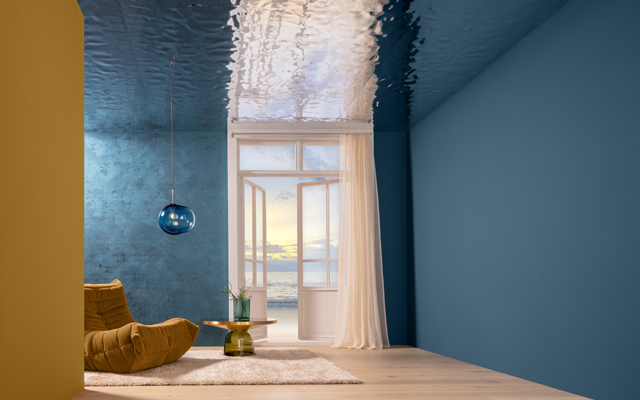 Ein Raum mit blauen Wänden. Ein offenes Fenster lässt Licht herein. In der Ecke steht ein beiger, bequemer Sessel und ein runder Tisch mit einer Pflanze.