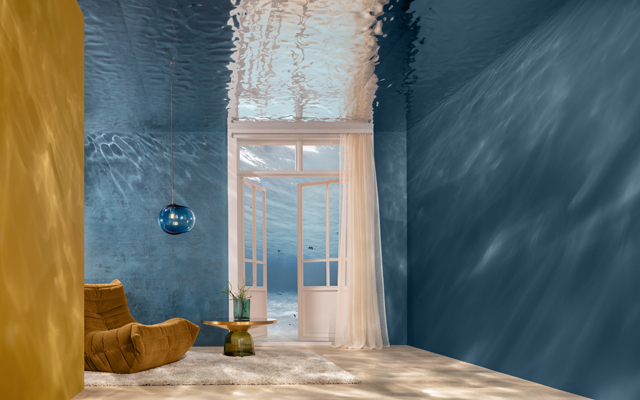 Ein Raum mit blauen Wänden. Ein offenes Fenster lässt Licht herein. In der Ecke steht ein beiger, bequemer Sessel und ein runder Tisch mit einer Pflanze.