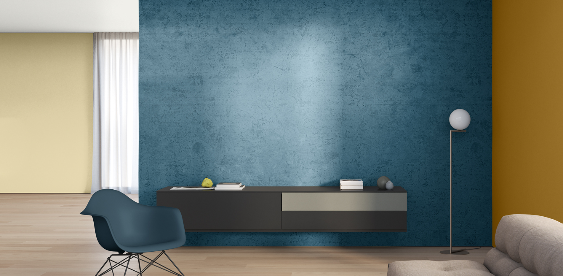 Ein modernes Wohnzimmer mit einer blauen Wand, einem dunkelbraunen Sideboard mit einer grauen Schublade. Links steht ein blauer Stuhl und rechts ein Stehlampe mit einem runden Lampenschirm.